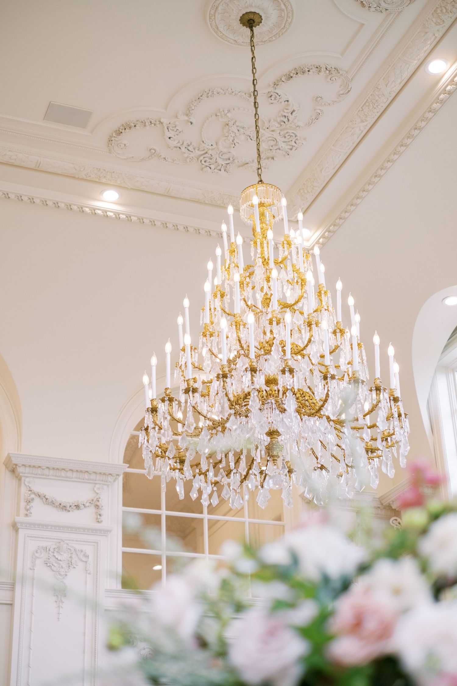 Grand crystal chandelier sparkles against ornate white ceiling with decorative moldings.
