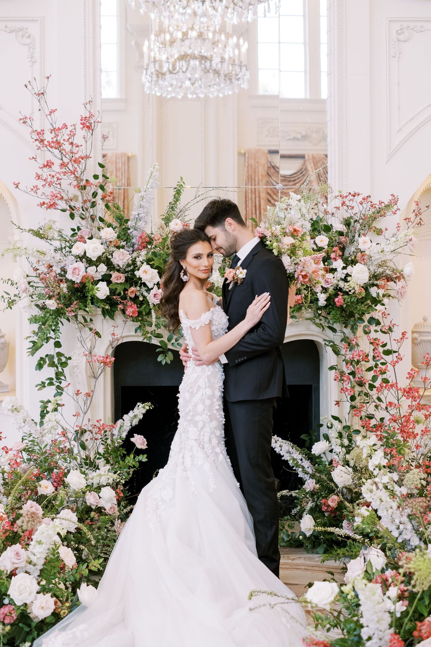 A romantic wedding scene with floral arch arrangements and chandelier in an elegant white room.