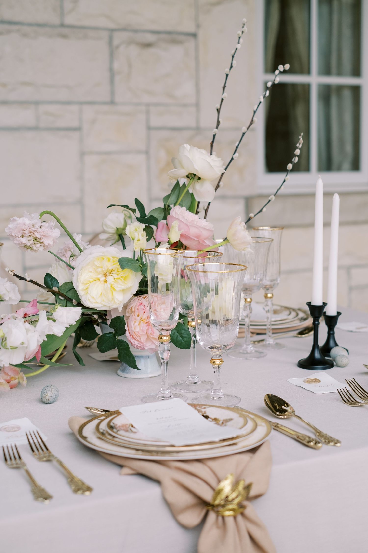 An elegant table setting with pink flowers, crystal glasses, and gold-rimmed plates.