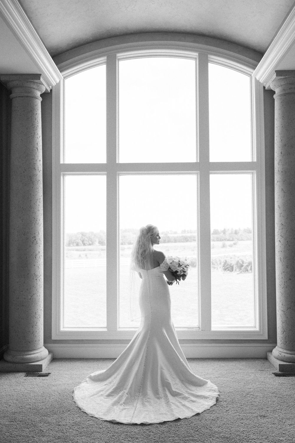 Black and white bridal portraits showcasing wedding dress details against architectural windows.