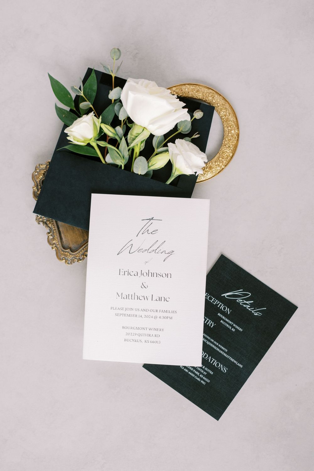 Wedding stationery flat lay featuring black and white cards with gold details and white roses.