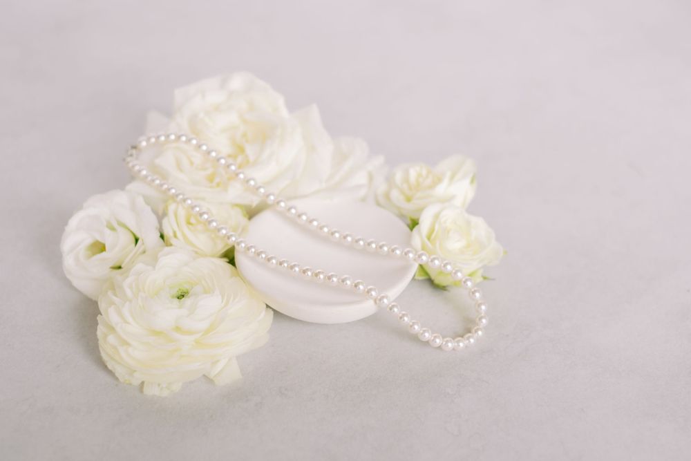 White ranunculus flowers with pearl necklace arranged on light gray background.