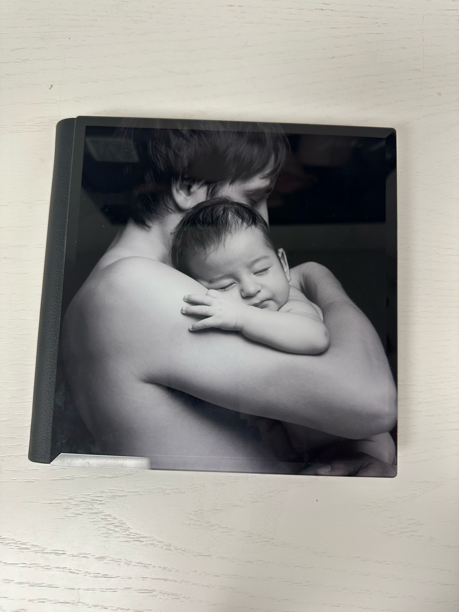 Black and white photo book cover featuring a parent cradling a sleeping newborn baby against their chest. Photo book