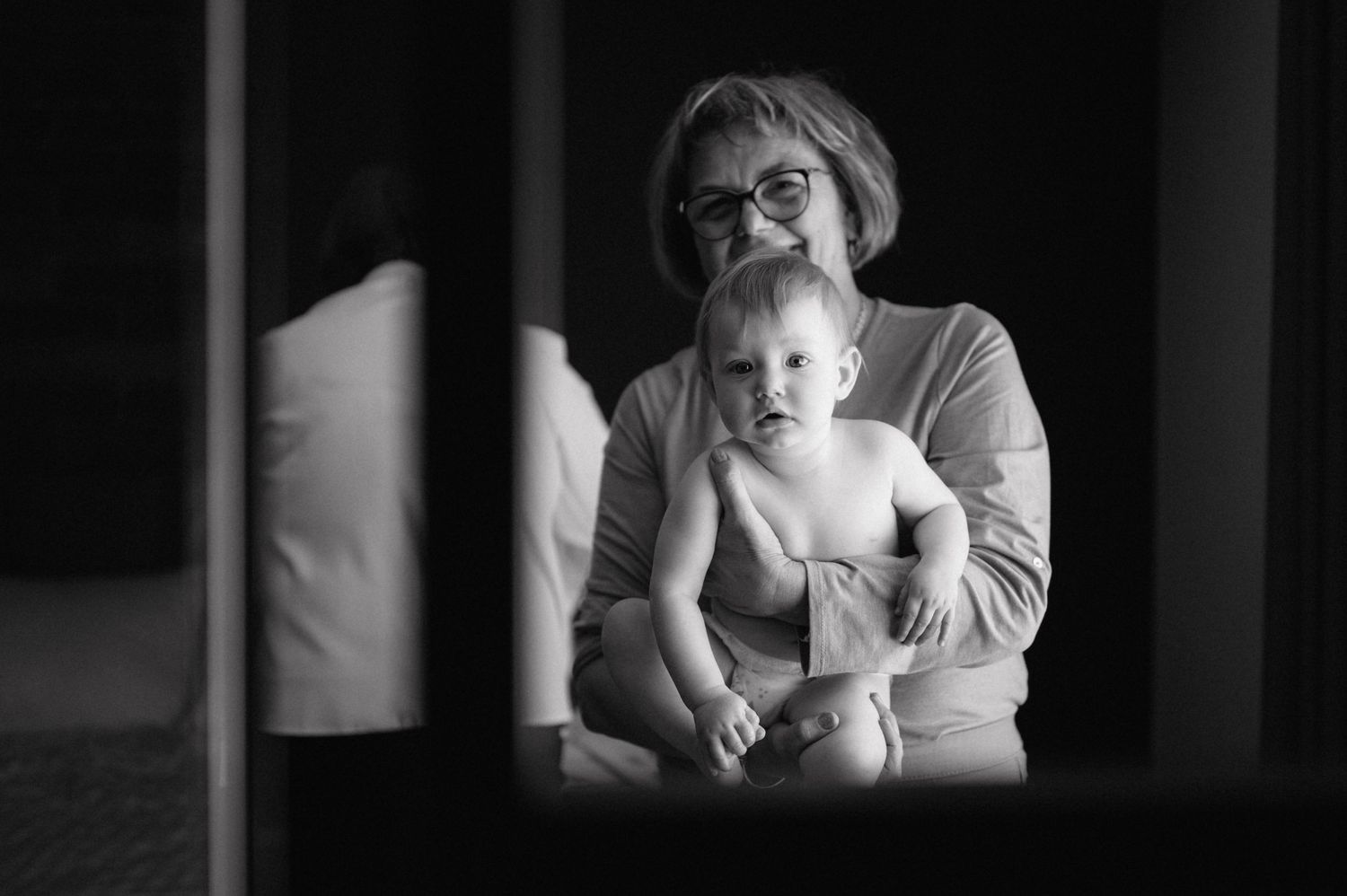 A black and white photograph captures a tender embrace between an adult and young child in moody lighting.