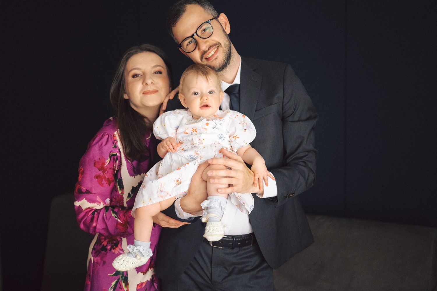 A family poses together against a dark background wearing formal attire including a pink dress and dark suit.