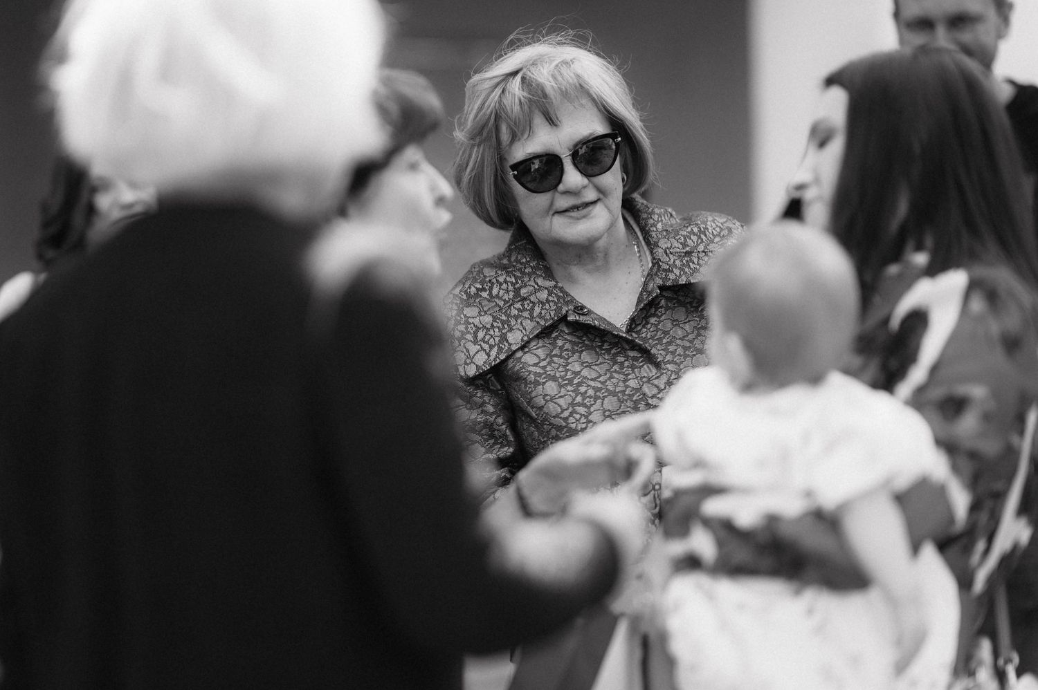 A black and white photo of people gathered at a social event with someone wearing sunglasses in the center.