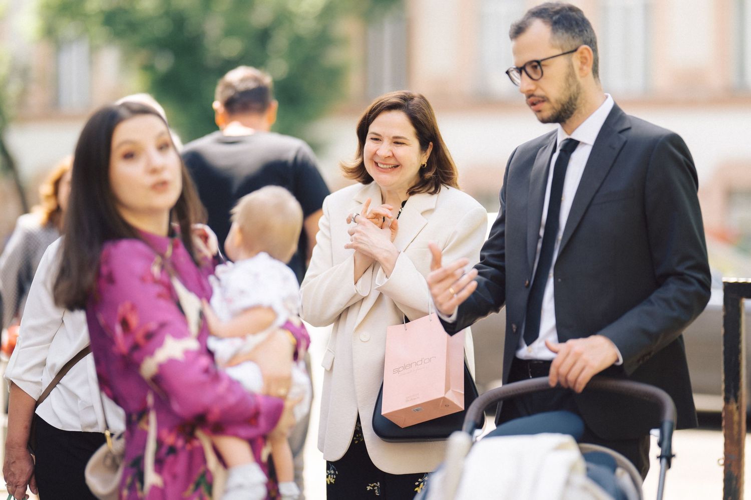 A group of people interact outdoors while holding shopping bags and strolling together in an urban setting.