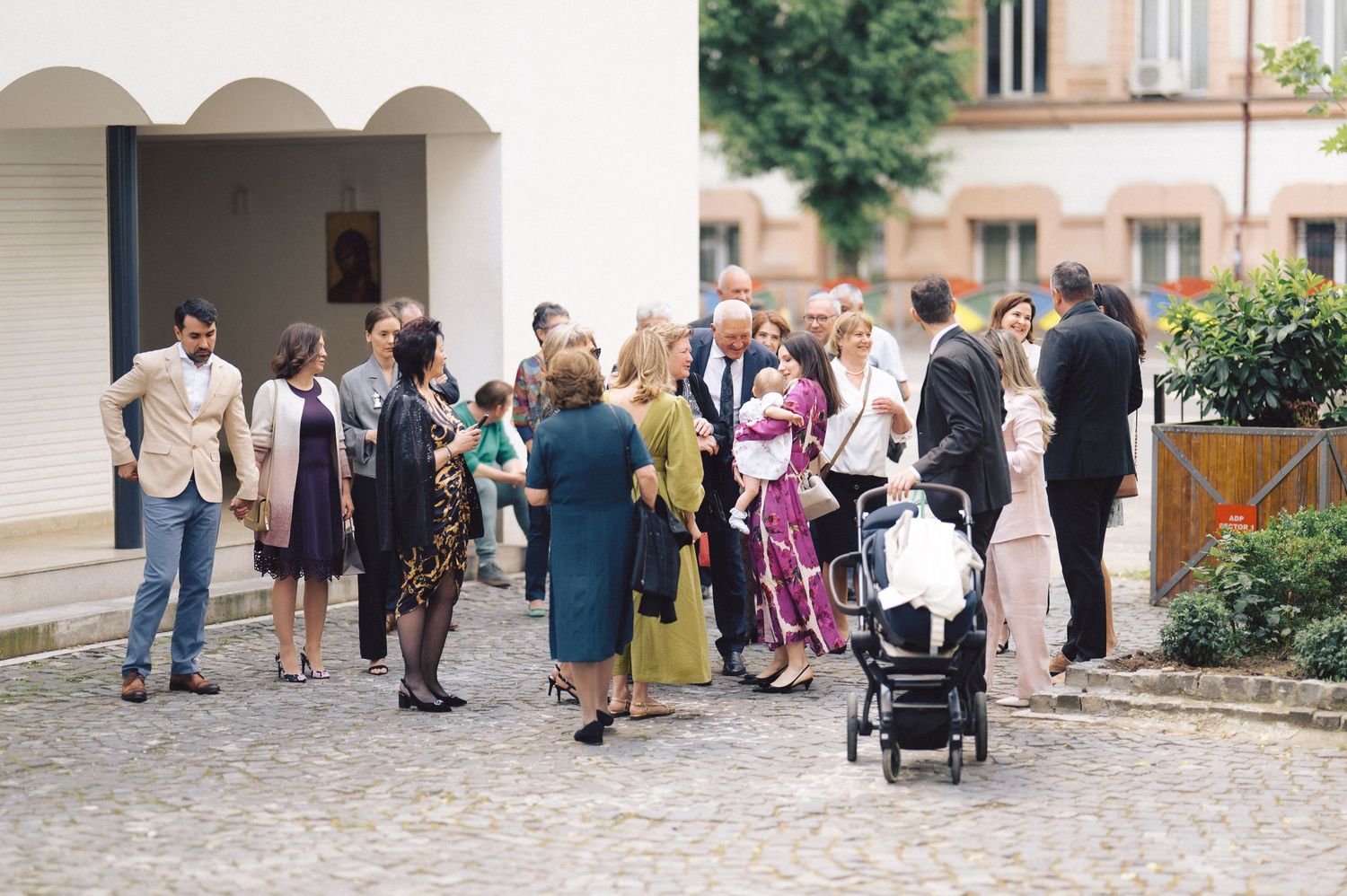 A group of formally dressed guests gather outside for a social event on a cobblestone courtyard.