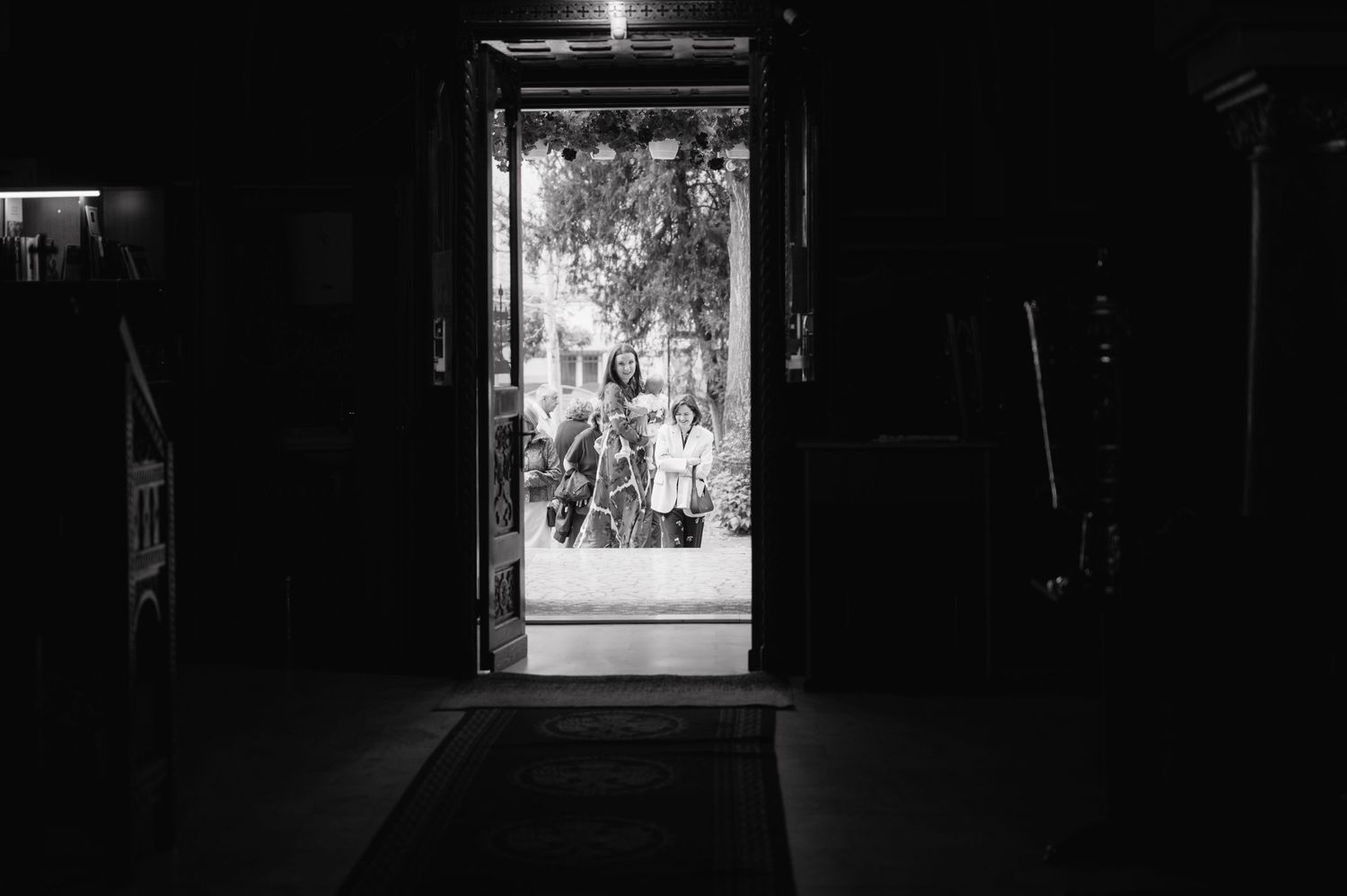 Dark interior with bright doorway framing a crowd of silhouettes visible through the illuminated entrance.