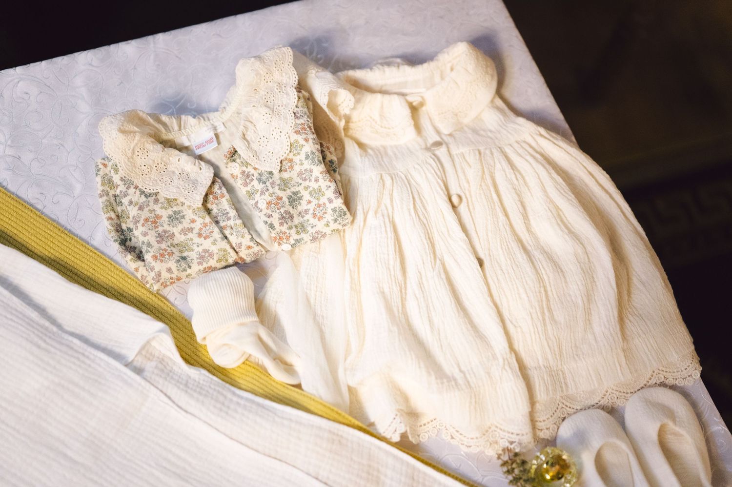 A delicate vintage white baby dress with lace details and embroidery laid out on fabric.