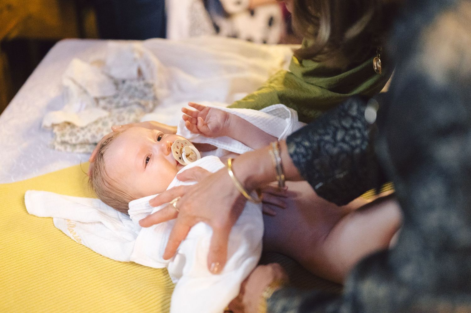 A baby lying on a yellow surface while being gently touched by caring hands.