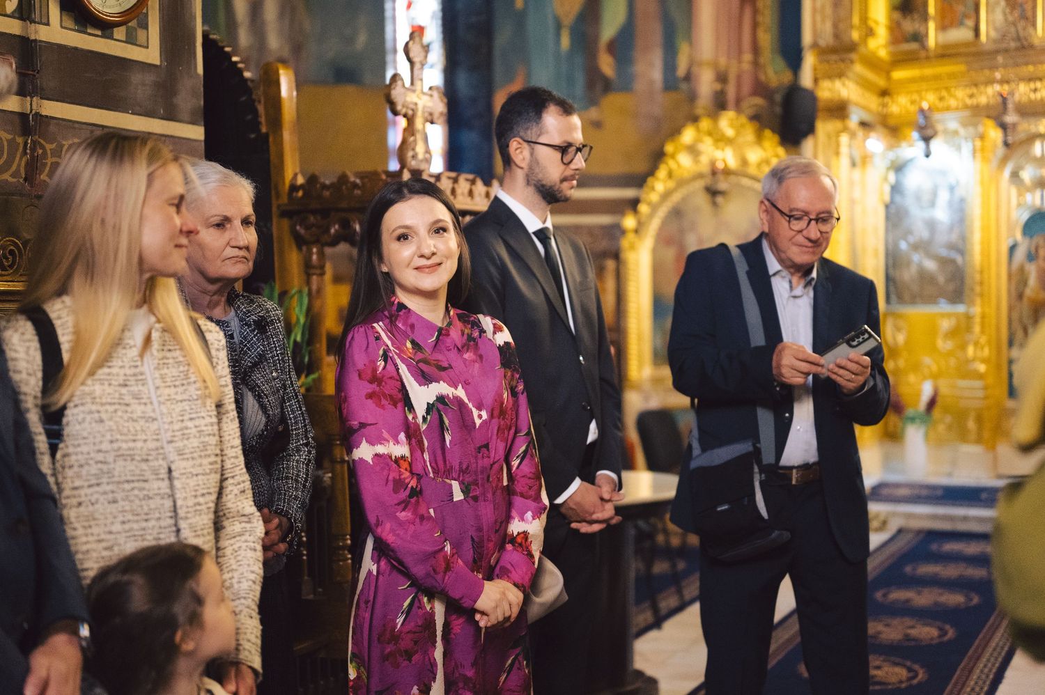 A group of people stand in a grand ornate space with gold decor as they attend what appears to be a formal gathering.