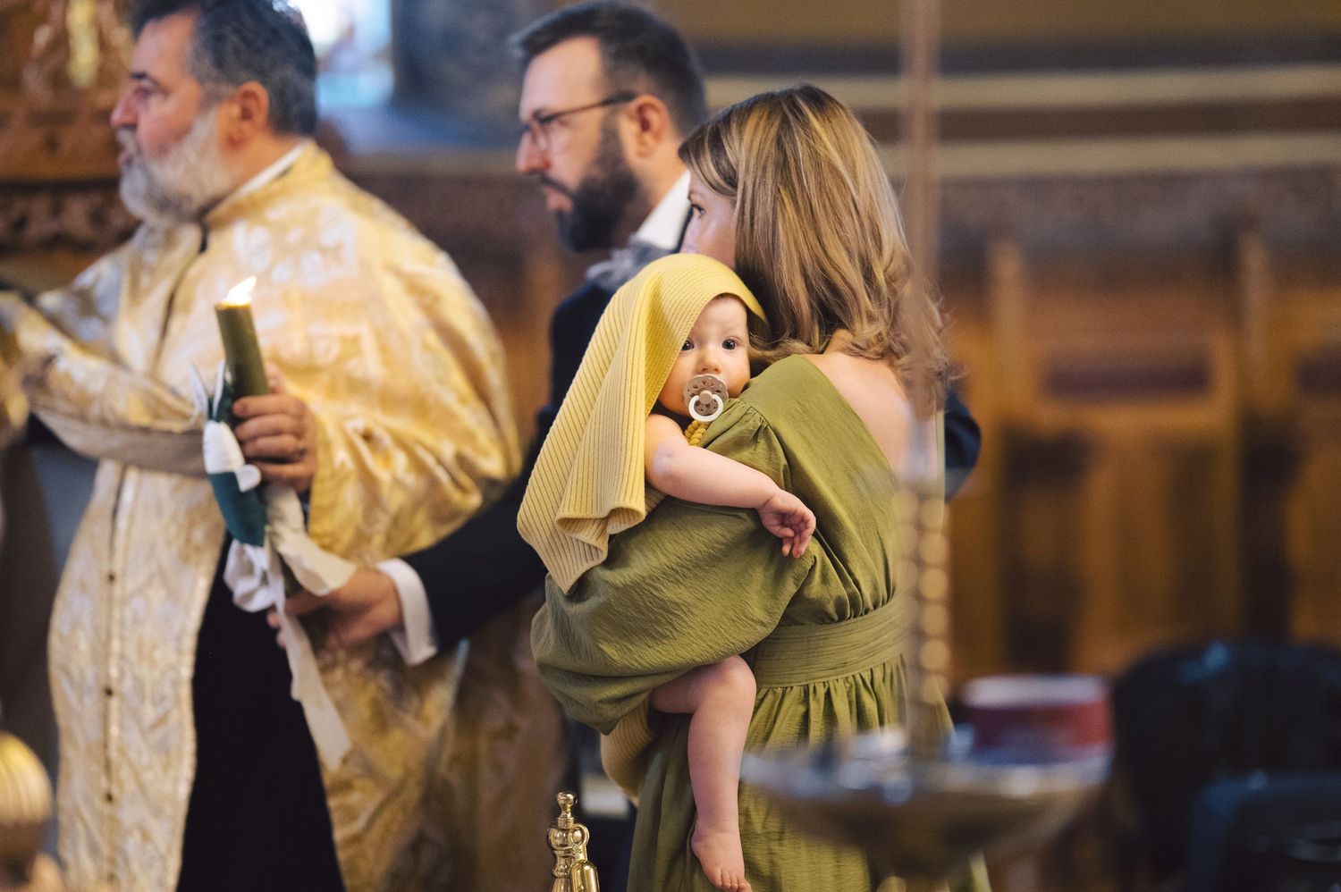 A baptism ceremony in progress at a church with clergy members and participants in formal attire.