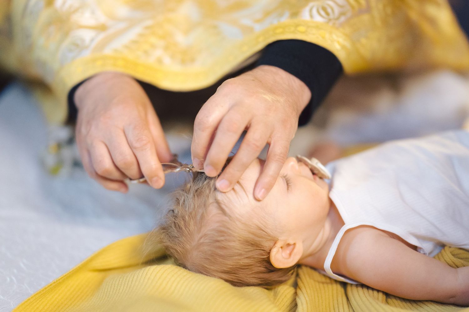 Parent gently checking infant's temperature with thermometer while baby lies on yellow blanket.
