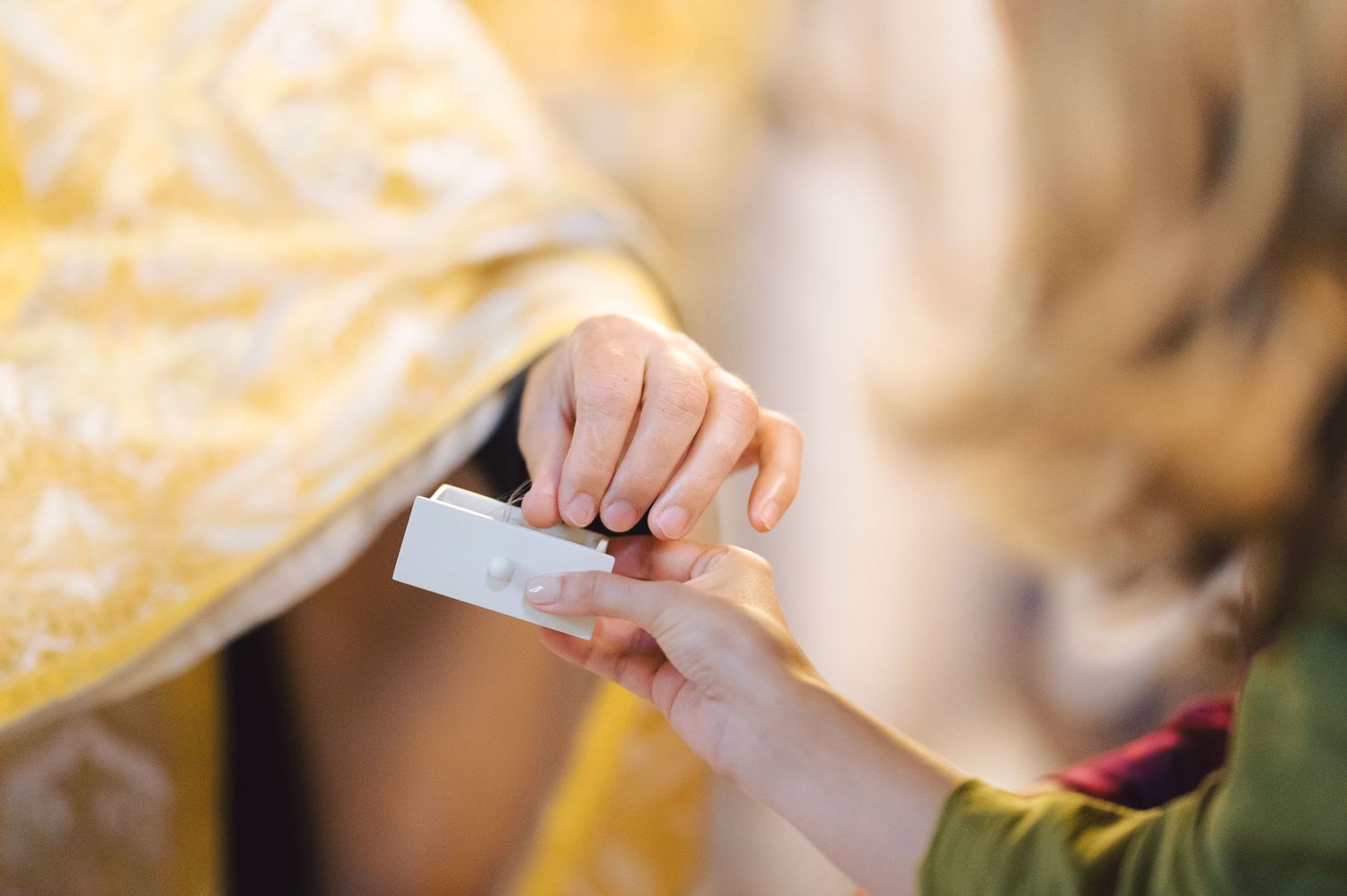 A priest applies holy oil during a religious ceremony using a small silver instrument.