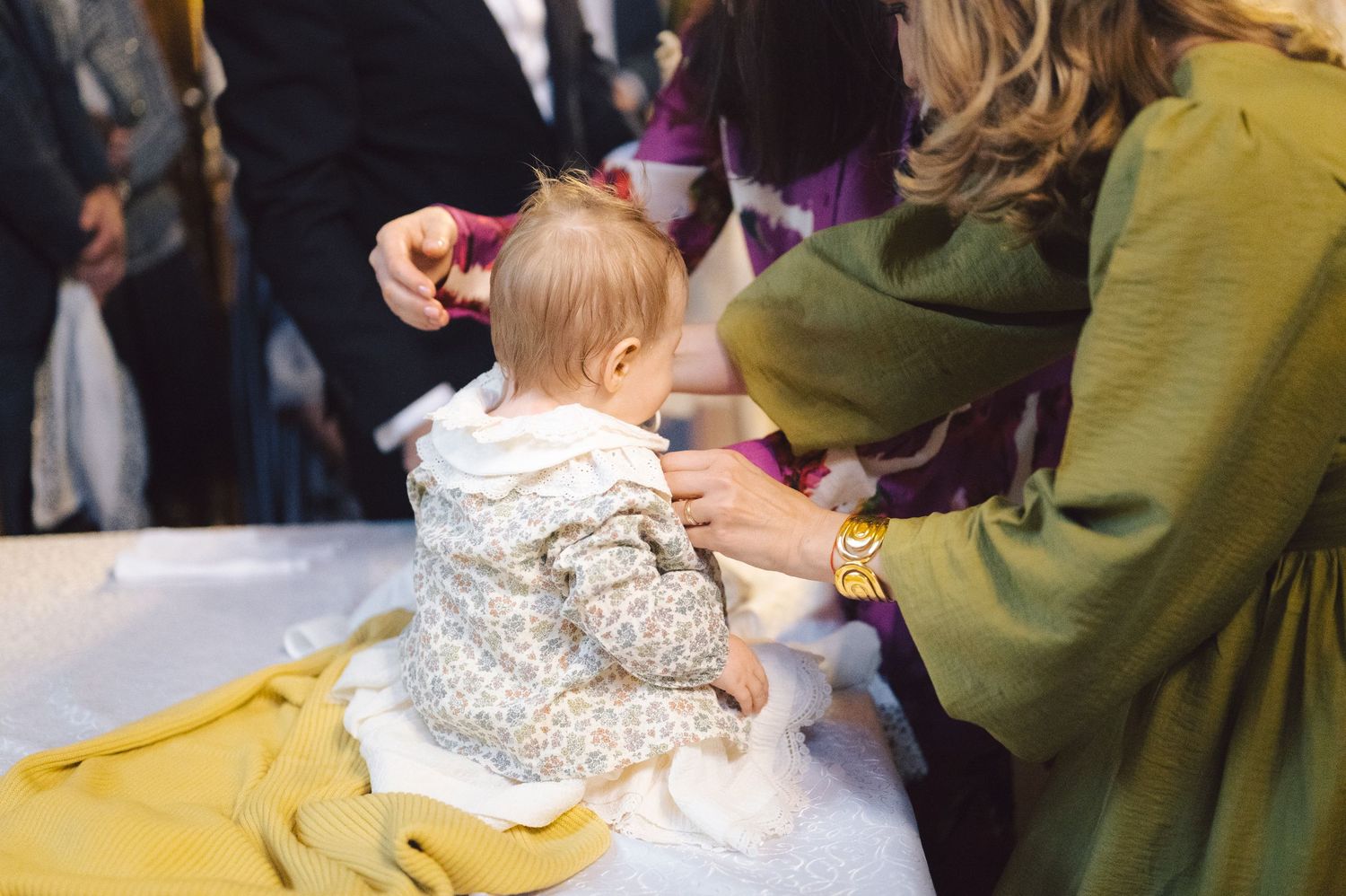 Baby wearing floral outfit sits on yellow blanket while receiving medical care.