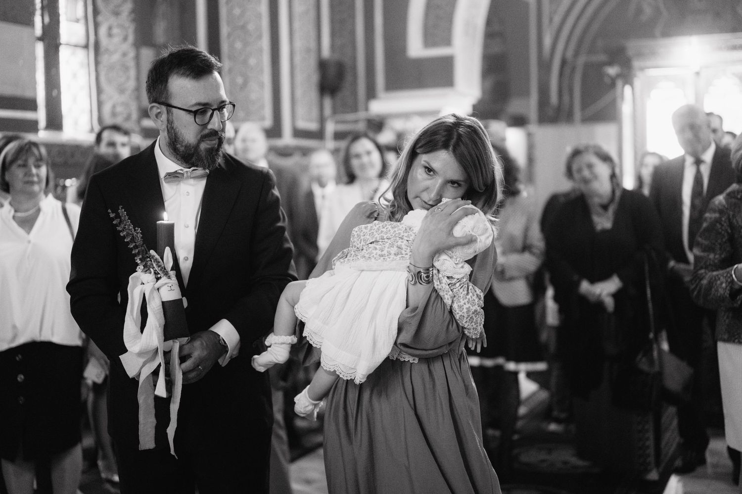 A sweet baptism ceremony taking place in a traditional church with a baby in a white christening gown.
