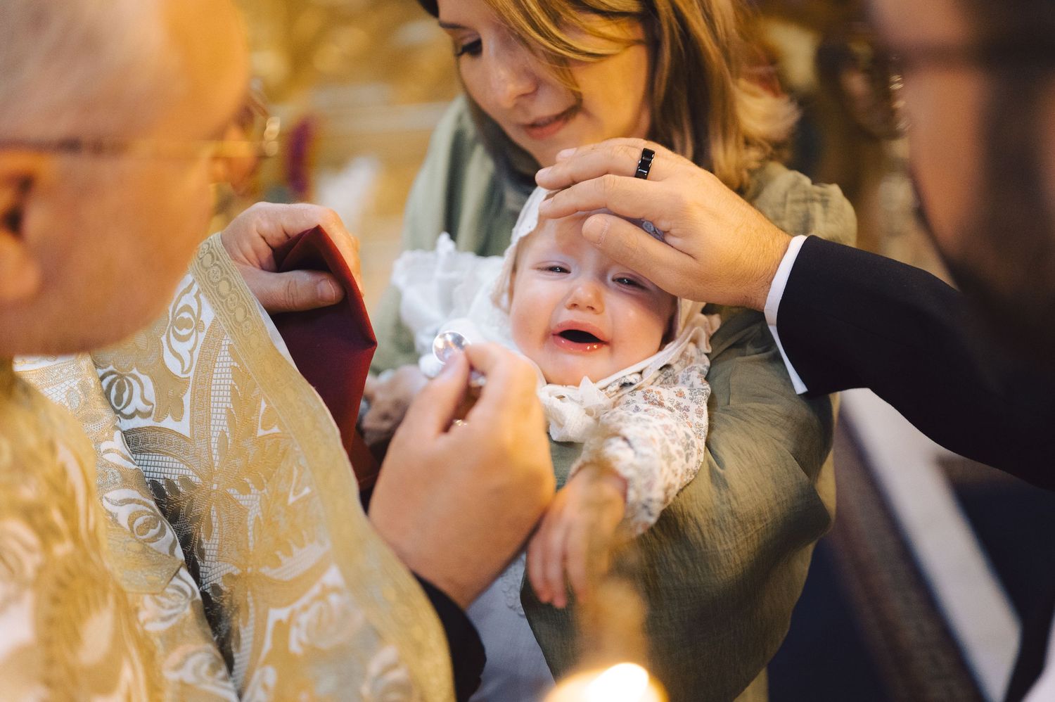 A baby in white christening gown cries during a traditional baptism ceremony in church.