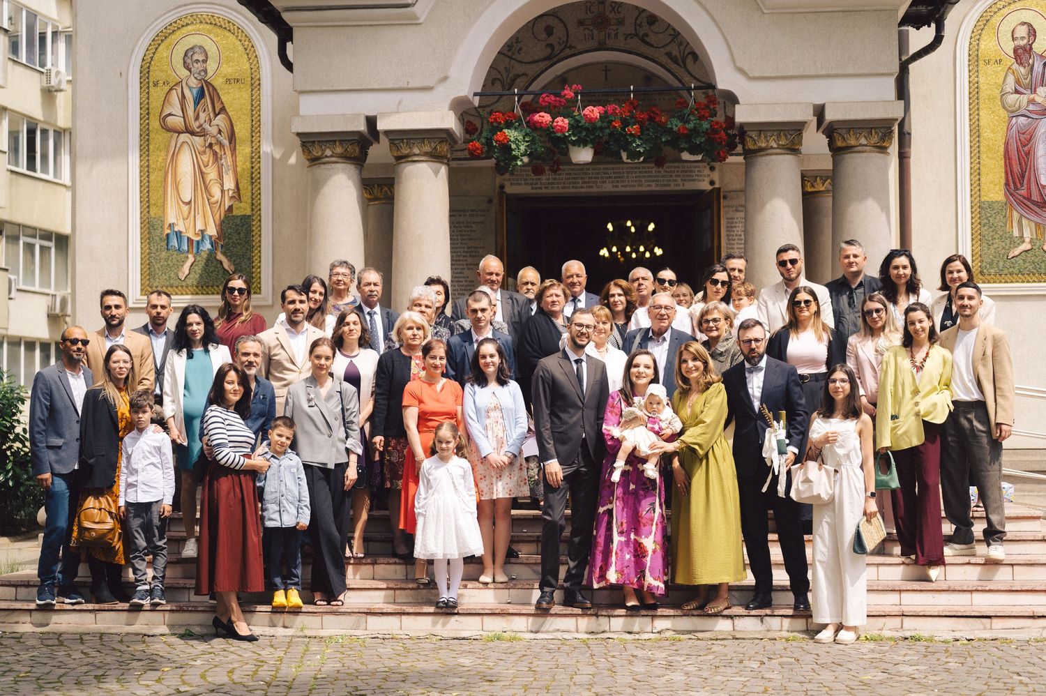 Large group photo of dressed-up guests gathered on church steps after a religious celebration in front of ornate arches.