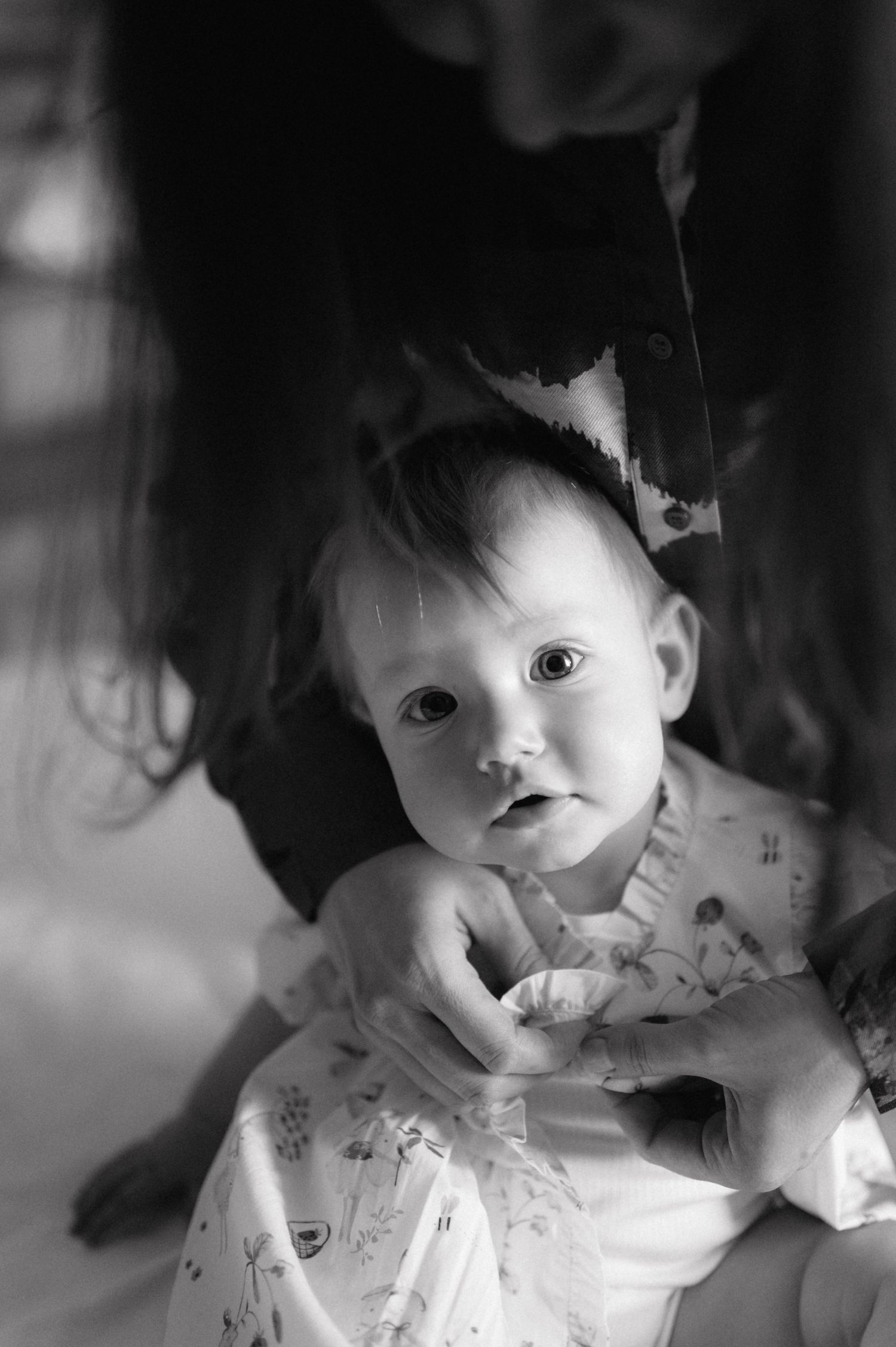 A captivating black and white portrait of an infant in patterned clothing looking at the camera with wide eyes.