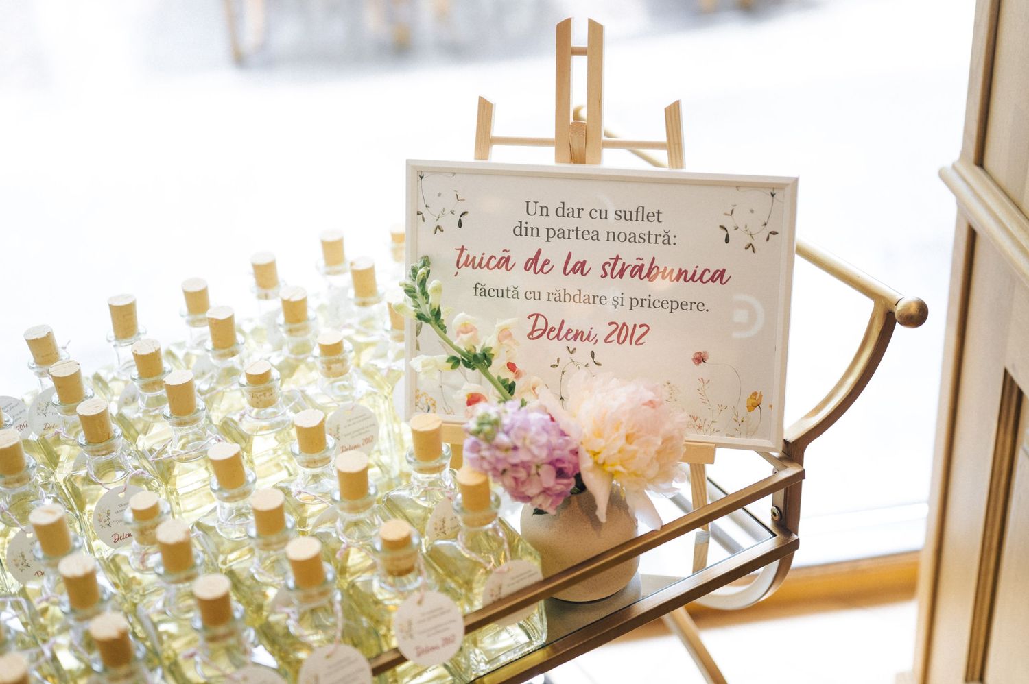 Rows of small glass bottles with cork stoppers arranged as wedding favors next to a decorative sign in natural light.