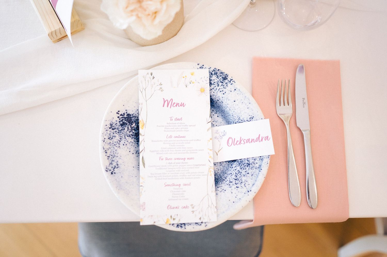Elegant place setting with blue marbled plate, coral pink placemat, and white menu card on a light table.