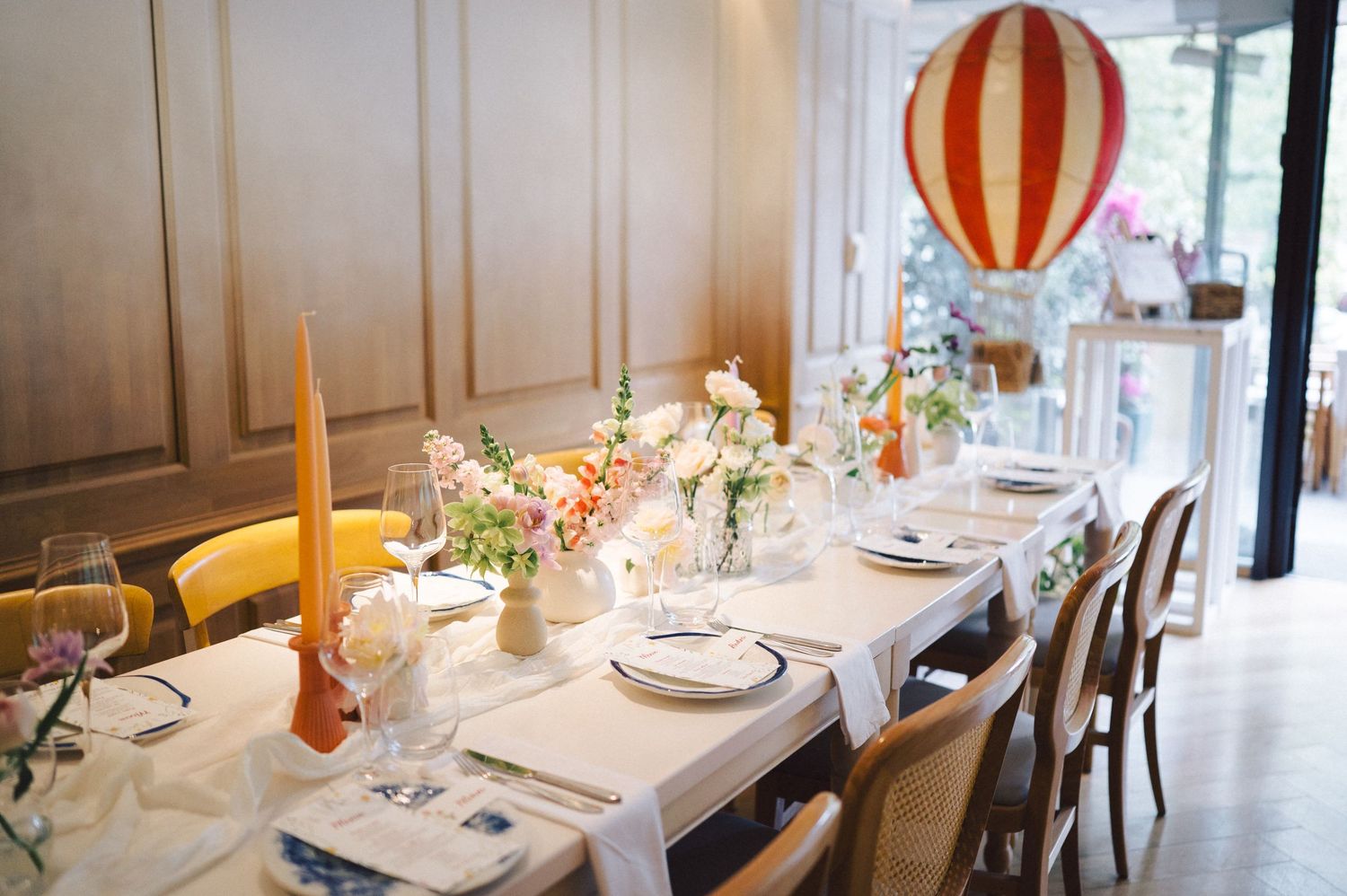 An elegant table setting with tall yellow candles, small floral centerpieces, and a whimsical hot air balloon decoration.