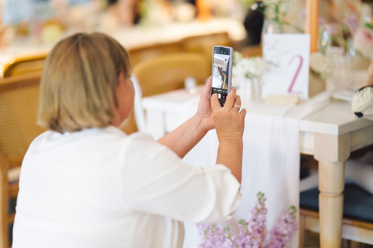 Someone takes a photo of wedding decor with a smartphone at an event table decorated with pink flowers.