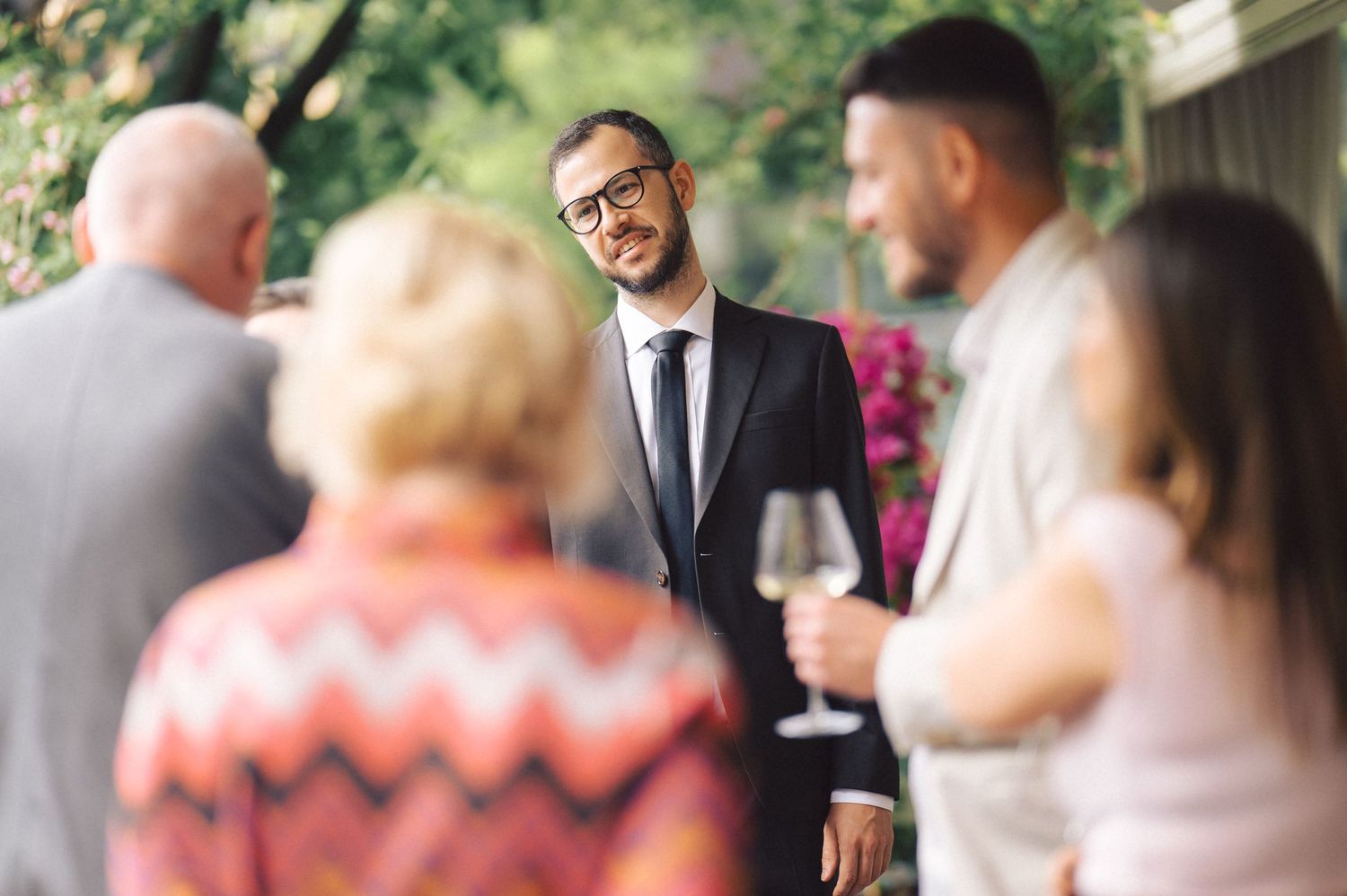 A group of people socialize at an outdoor gathering with wine glasses while enjoying conversation on a patio.