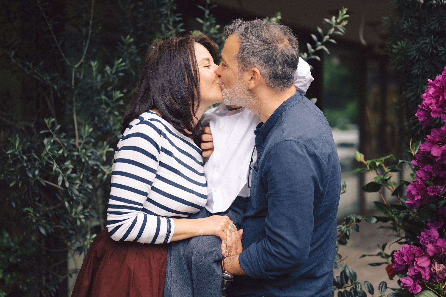 A couple sharing a romantic kiss in a garden with blooming pink flowers in the background.