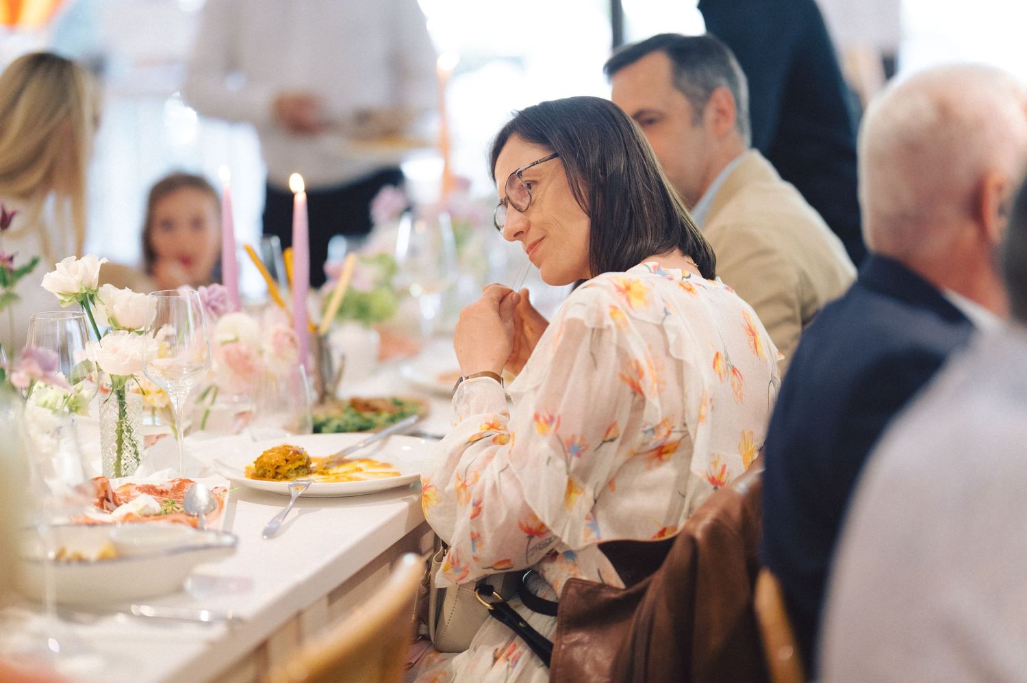 Guests enjoy an elegant dining experience at a formal event with candlelit table settings and floral decorations.