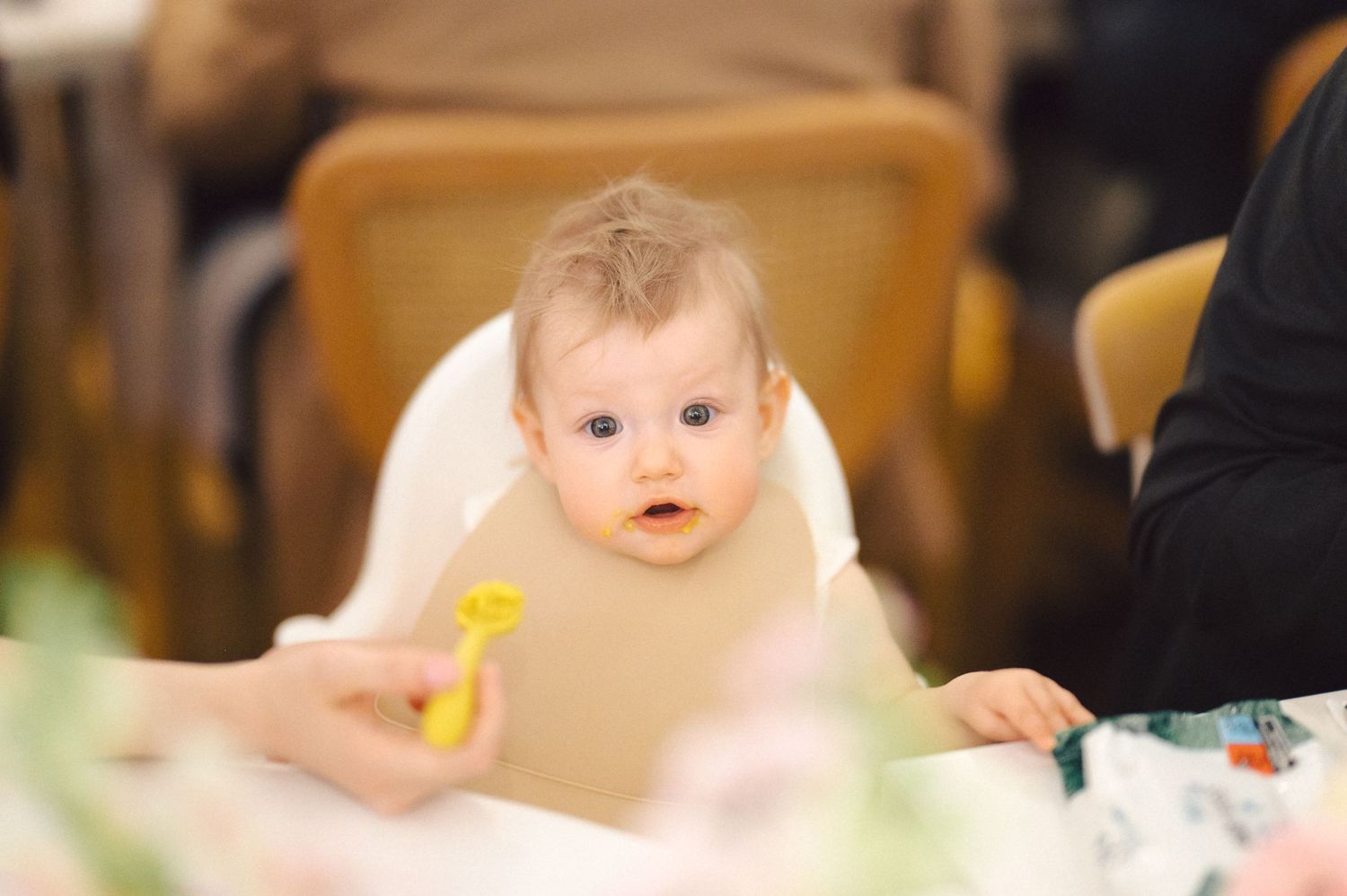 Baby sitting in high chair with a yellow toy during mealtime.