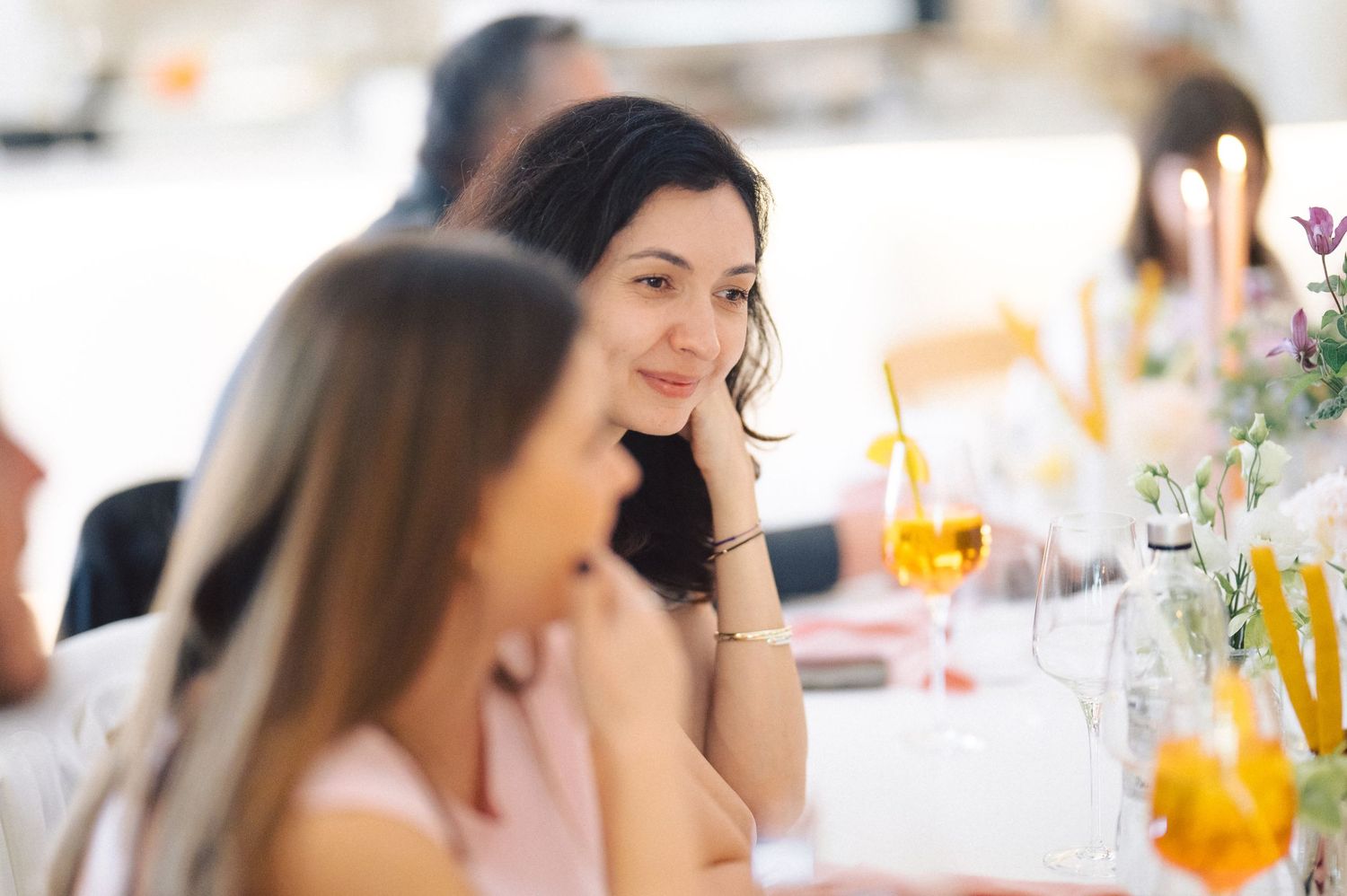 Guests enjoy refreshments and conversation at an elegant table setting with orange drinks and floral decorations.