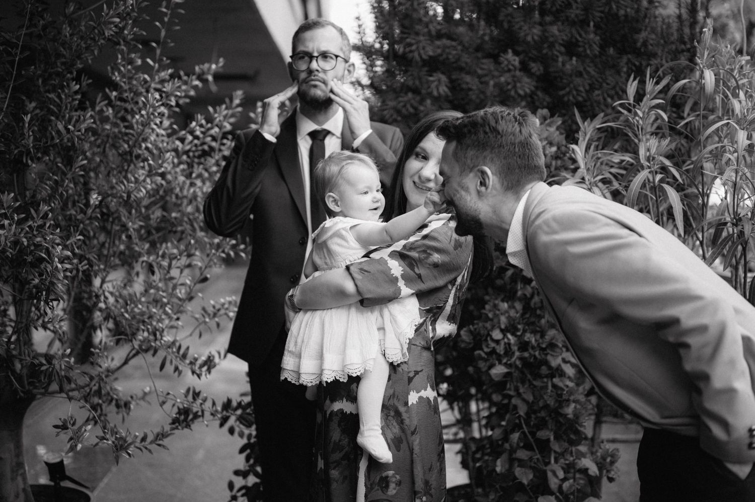 A vintage black and white photograph showing people interacting in a garden setting while dressed in formal attire.
