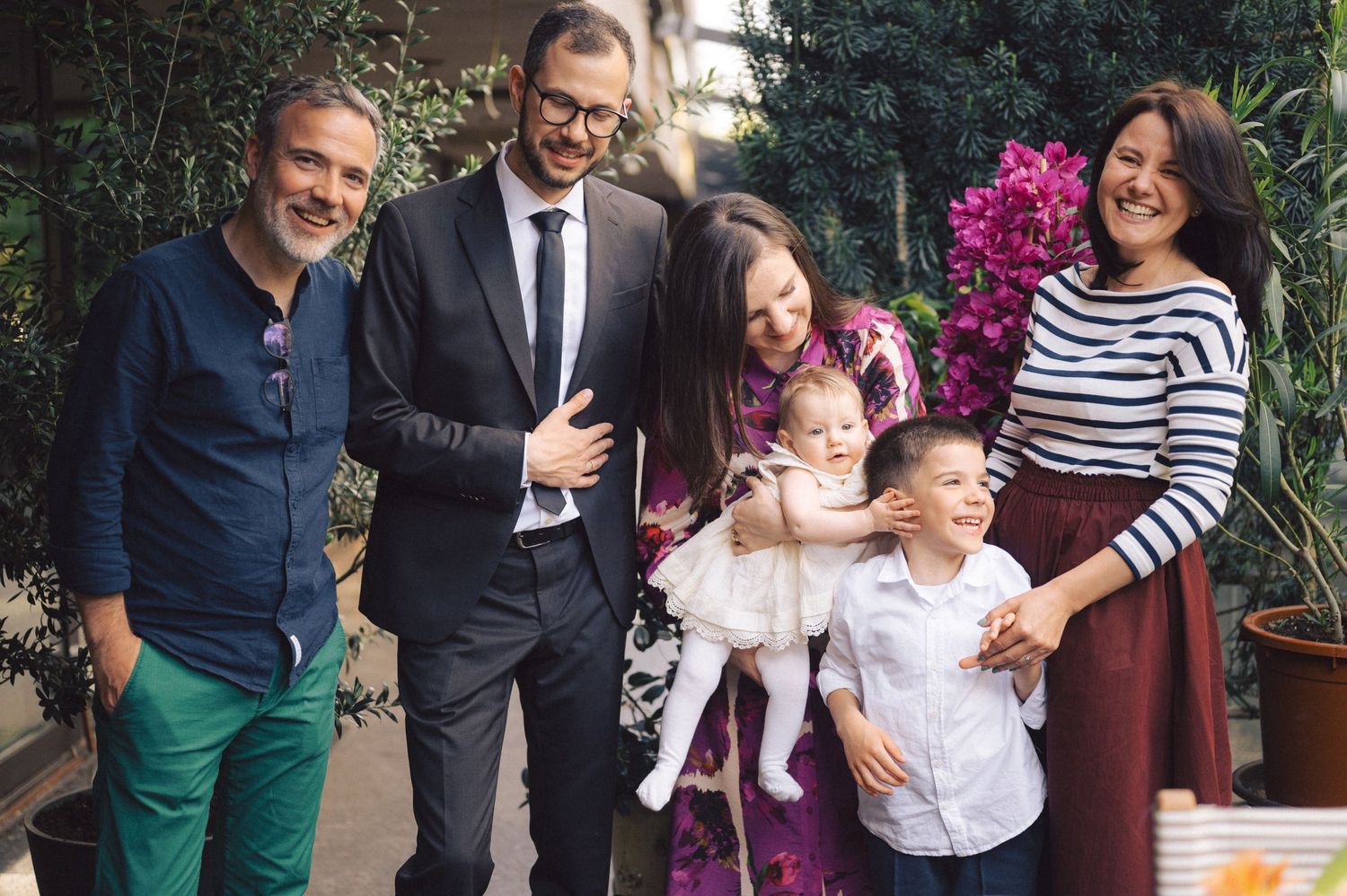 A cheerful group stands together outdoors in a garden setting with blooming pink flowers in the background.