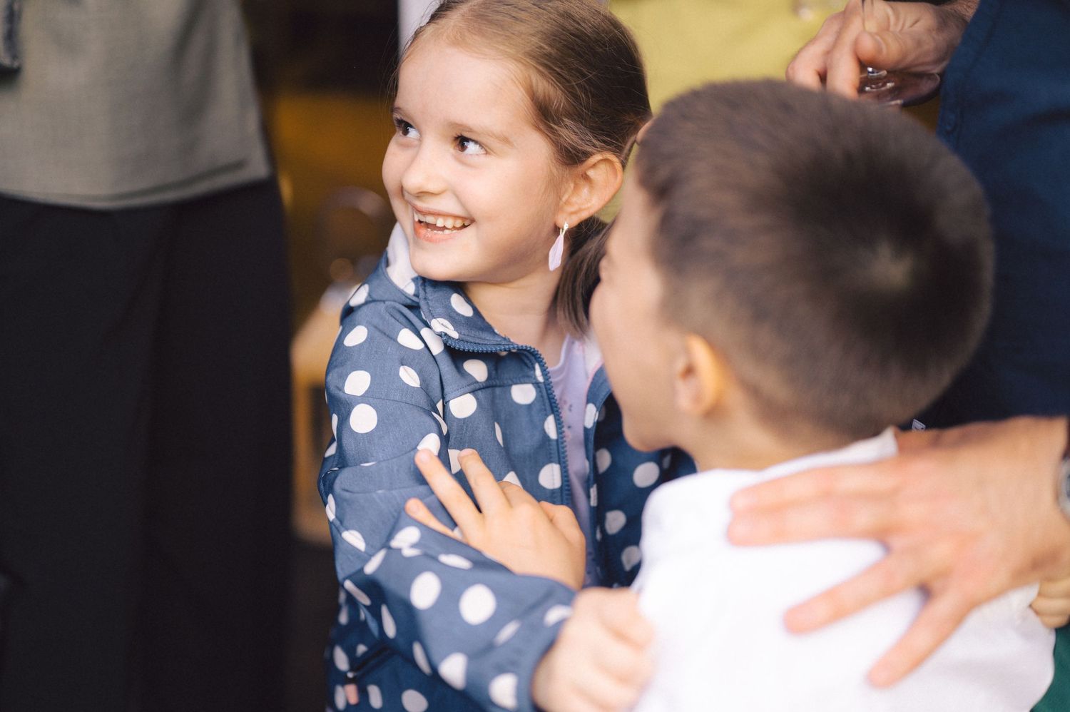 Two children share a joyful interaction while wearing casual attire at an indoor gathering.