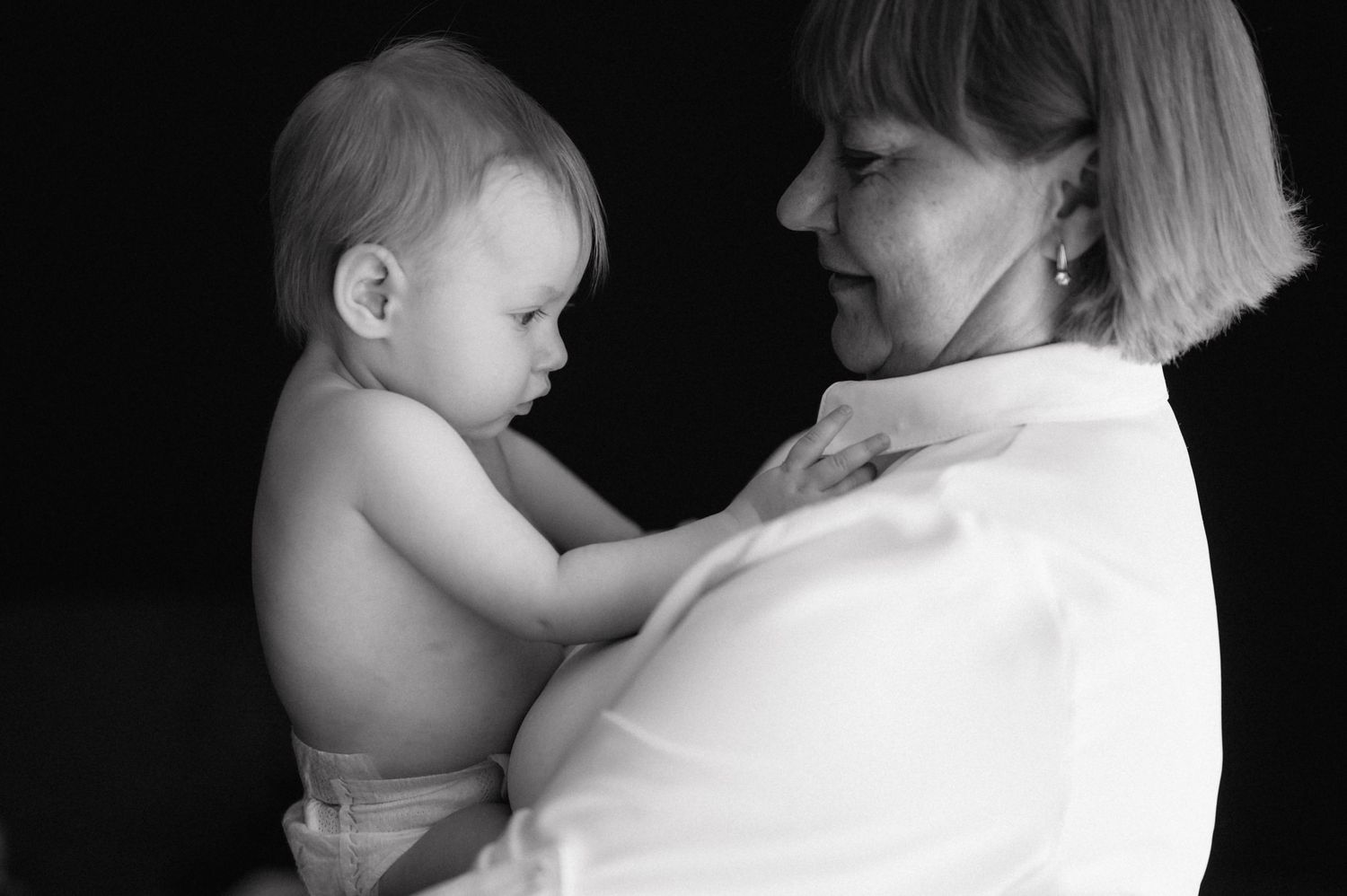 Black and white portrait of adult and baby in tender moment, baby wearing diaper and adult in white clothing.