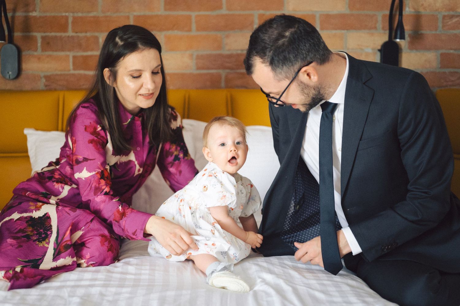 A family sits together at a restaurant table, while their excited baby in white clothing expresses joy.