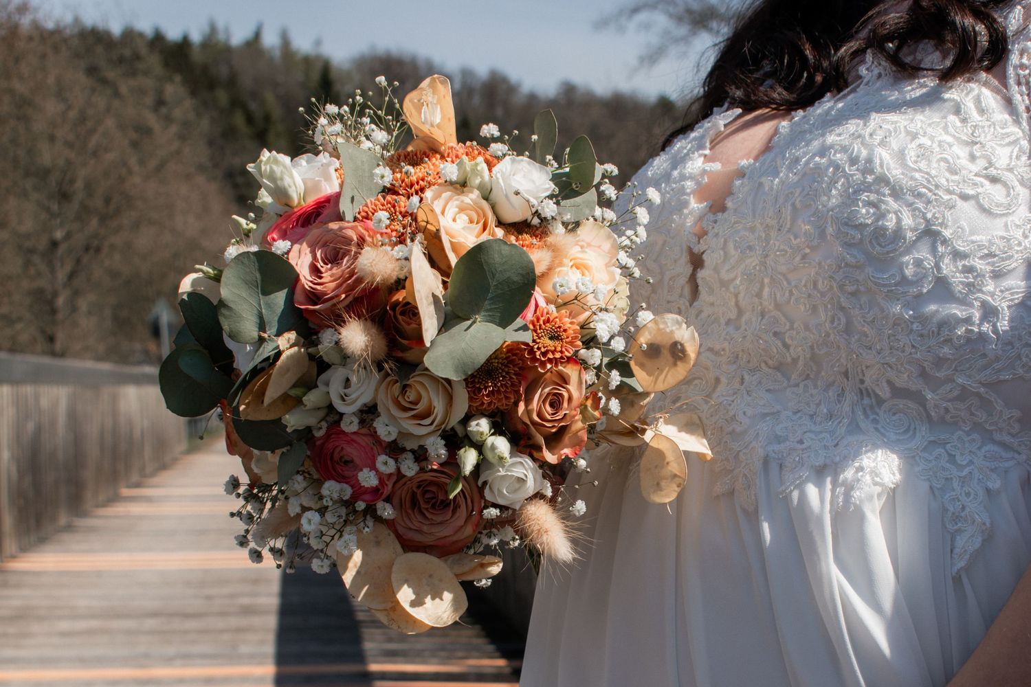 A smiling person wearing glasses and a white long-sleeve top poses outdoors on a sunny day with bare branches in background.