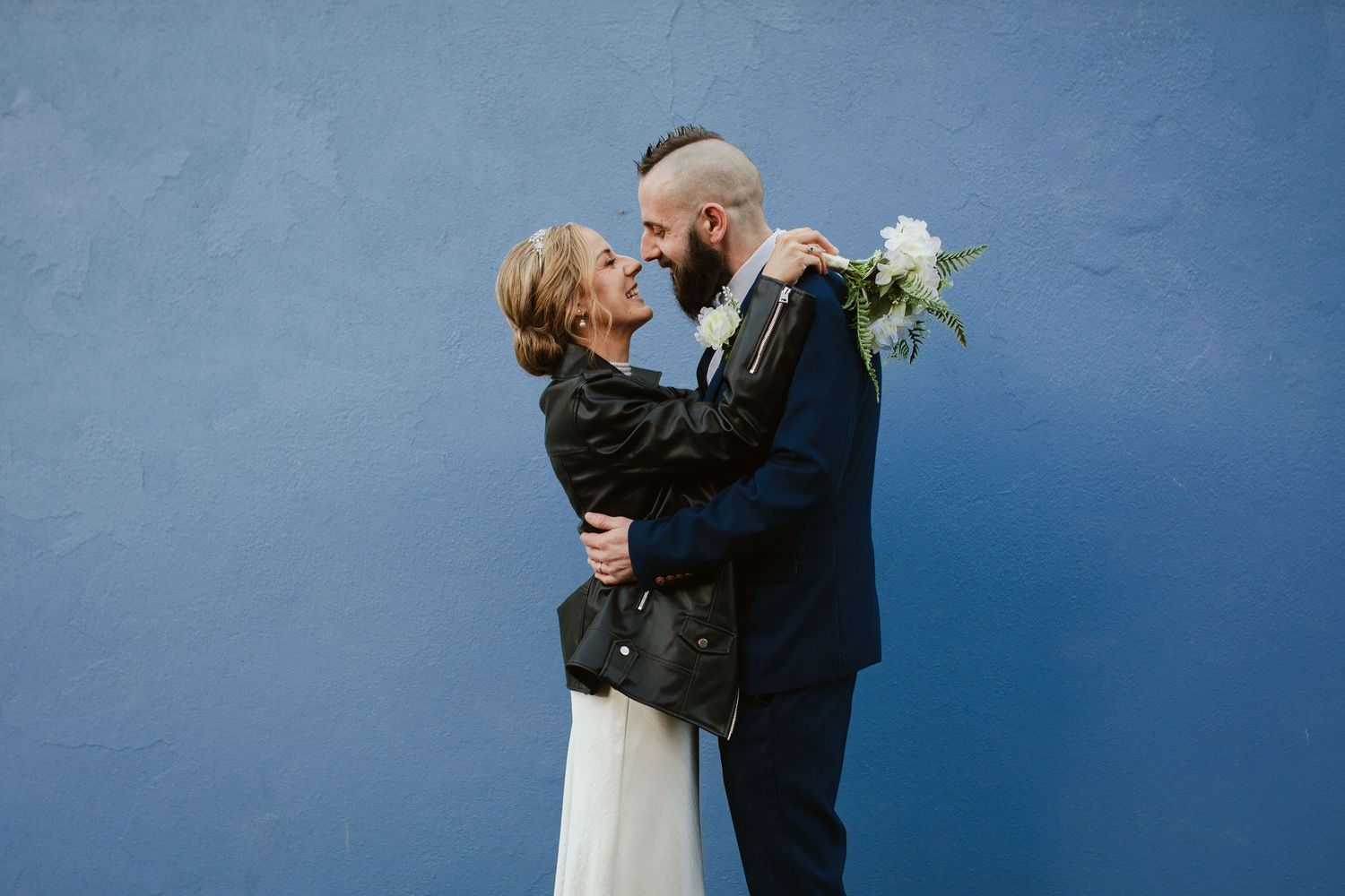 A couple embraces against a bright blue wall background during their wedding photoshoot.