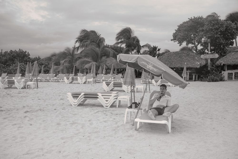 Black and white photo of beach lounge chairs and umbrellas on a tropical beach with palm trees swaying in the wind.Saint Maarten