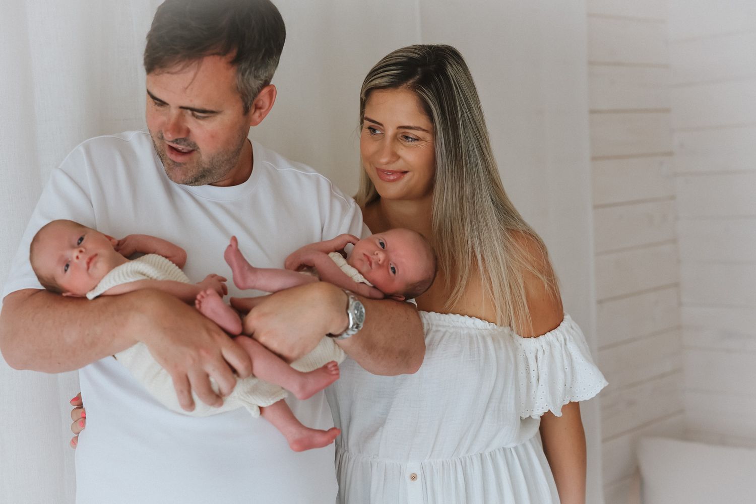 Black and white collage of newborn baby photography session with parents wearing white outfits in studio setting.