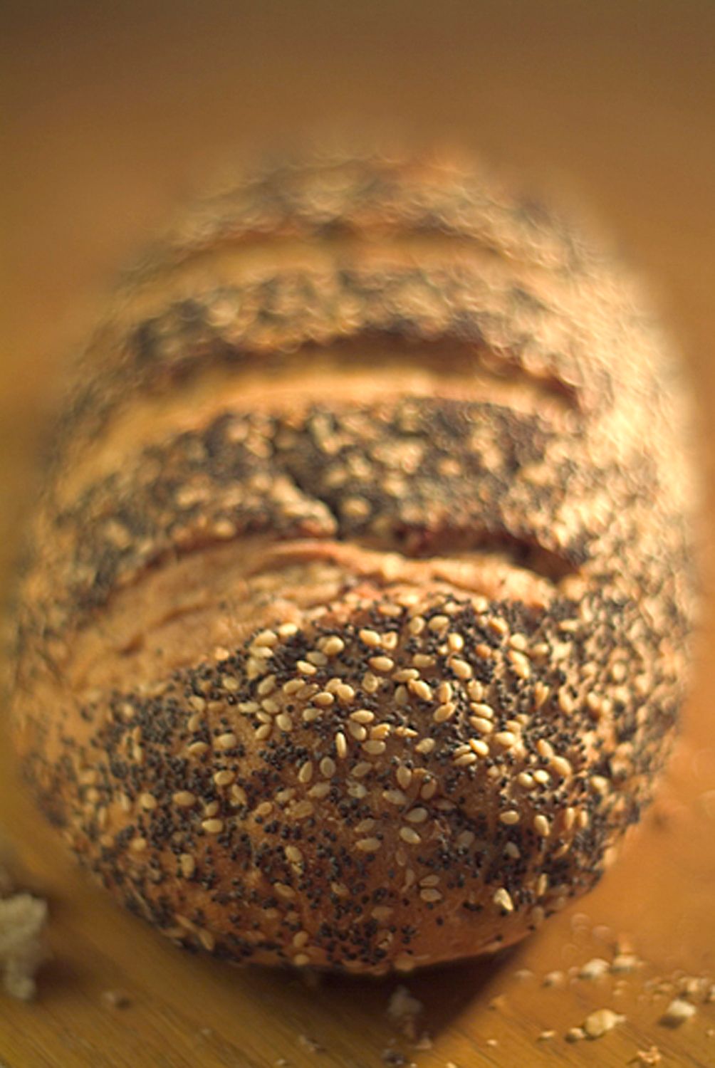 Close-up of a fresh dark bread roll covered in poppy and sesame seeds on a brown surface.