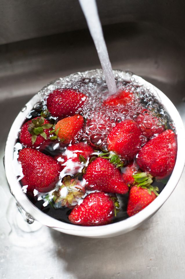 Fresh strawberries being washed under running water in colander.