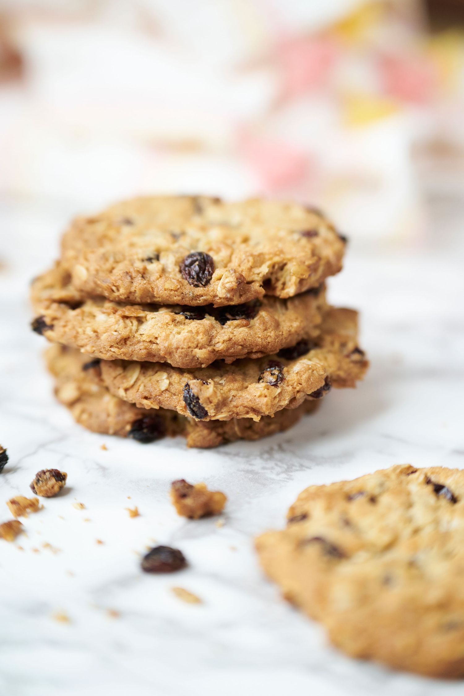 Stack of homemade oatmeal raisin cookies with crumbs on a white surface.