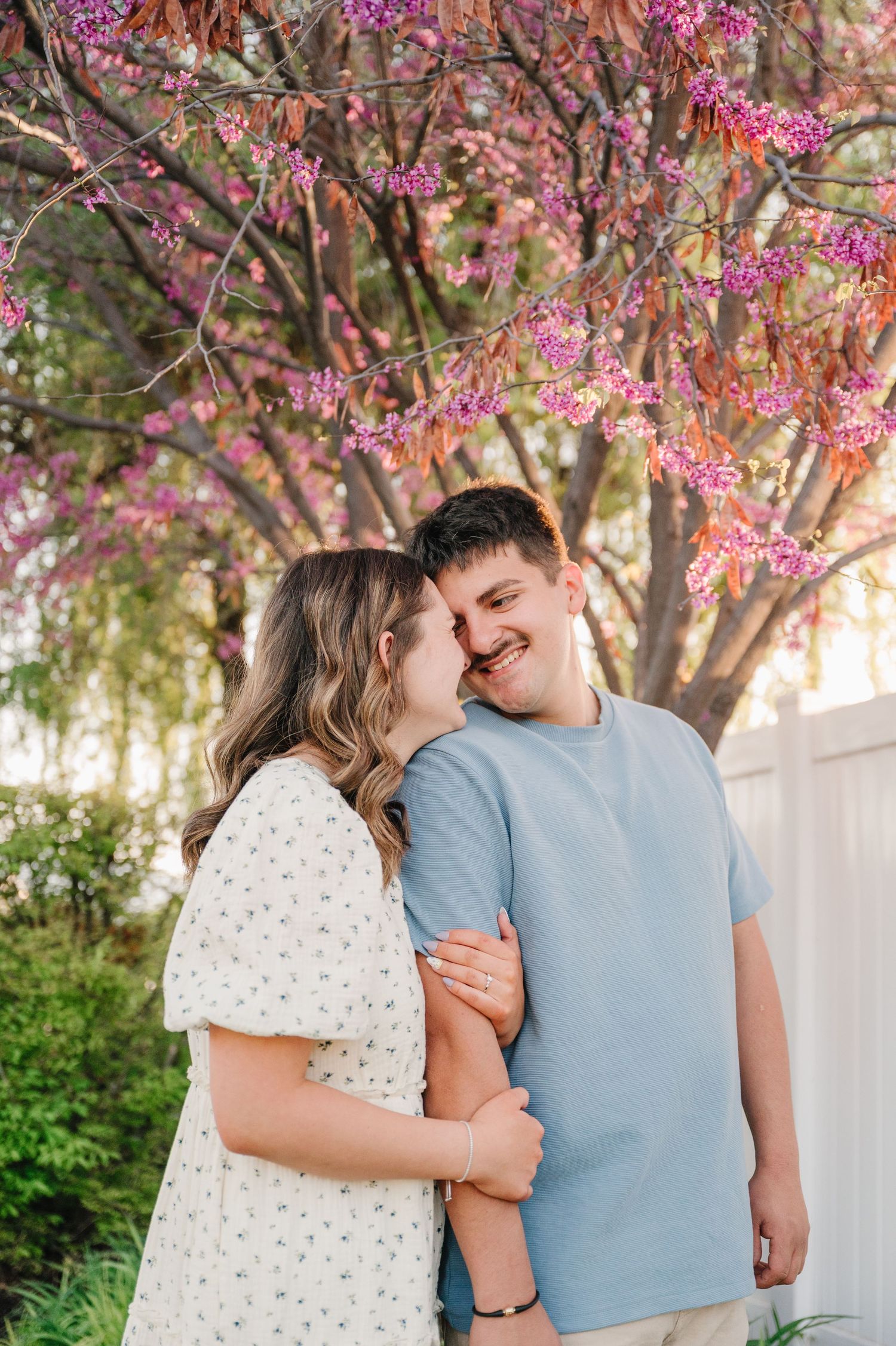 A couple shares a tender moment under blooming pink cherry blossoms in springtime.