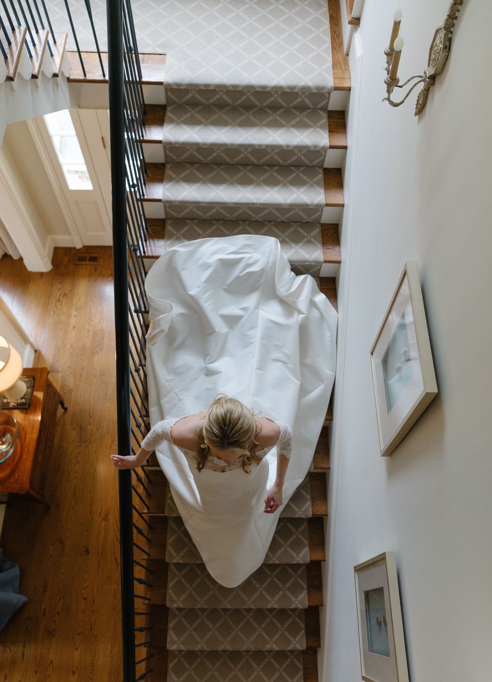 High angle view of a person in white wedding dress sitting alone on carpeted stairs in a home interior.