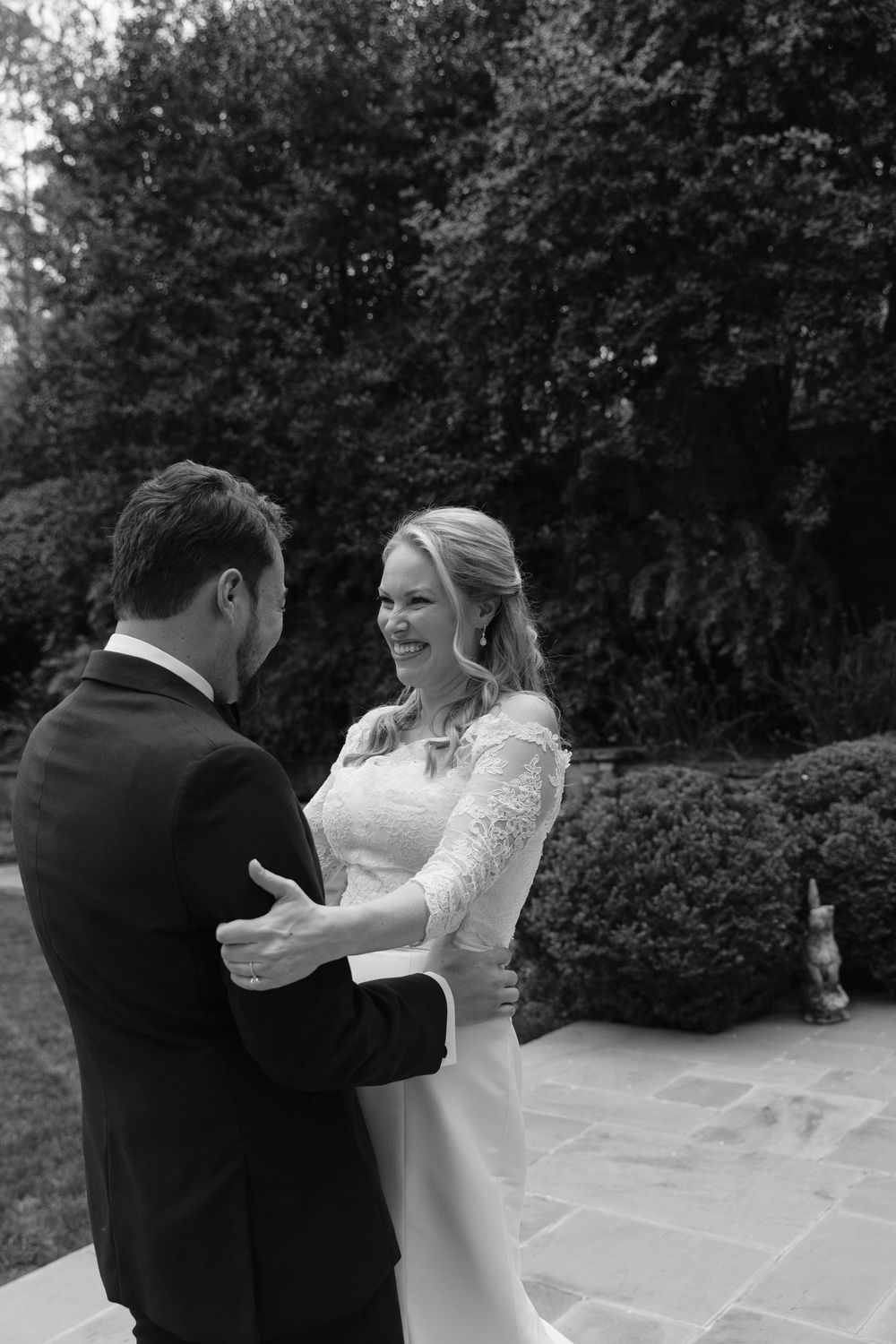 Black and white wedding photo of a couple dancing together on stone patio with garden in background.