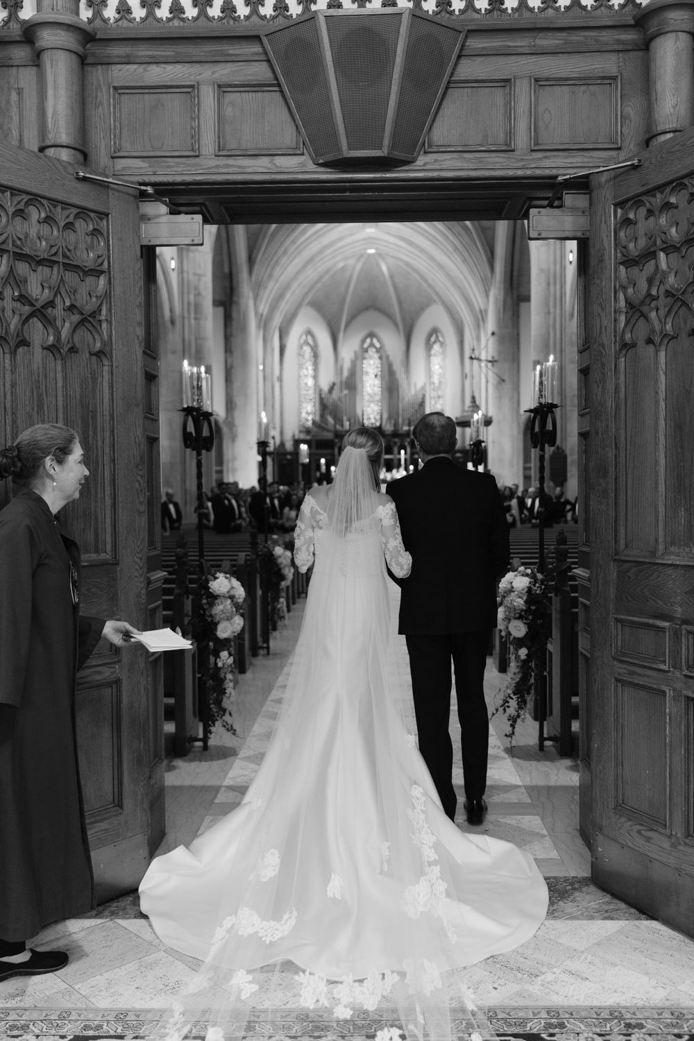 A bride and groom enter a grand cathedral church with vaulted ceilings and ornate wooden doors during their wedding ceremony.