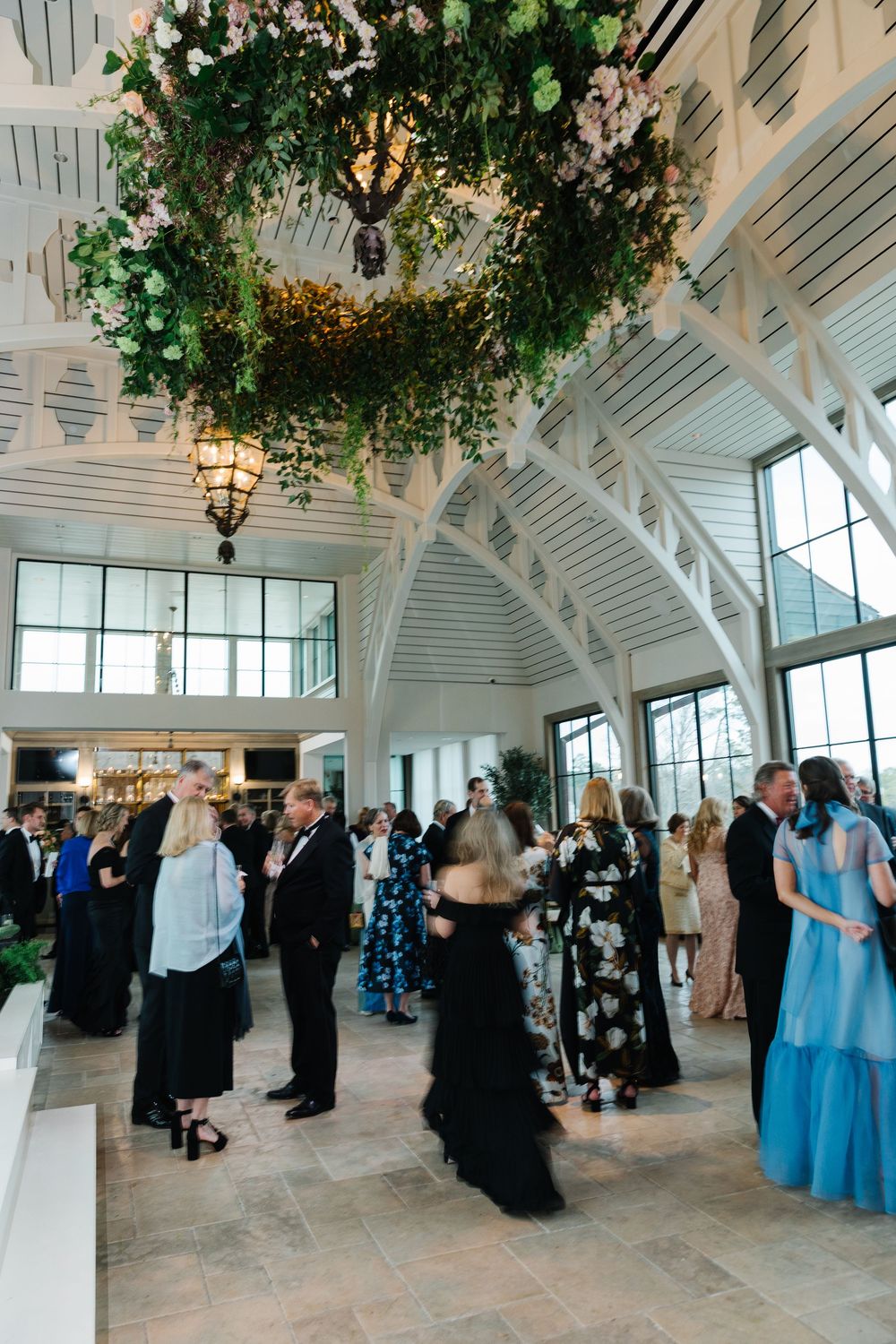 Elegant wedding reception in bright venue with vaulted ceiling and stunning floral chandelier above formally dressed guests.